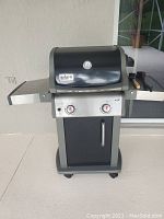 Full view of Weber Spirit black and stainless steel gas BBQ grill with two knobs and side shelves.