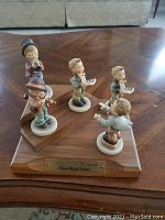 Photo showing the full 5 piece set of Hummel figurines on a wooden base with plaque