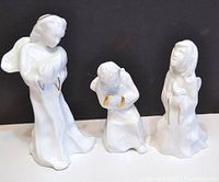 Three white ceramic angel figurines posed frontally showing design details.