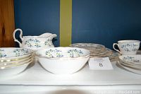 Photo showing multiple bone china dishes including cups, bowls, plates, and a gravy boat with floral Sonata pattern and gold edging arranged on a shelf.