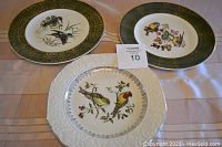 Two Wood and Sons 10 inch plates with green and gold borders featuring birds, and Stratford by Wood and Sons white plate with embossed edge and gold trim, all shown together on a surface.