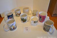 Photo showing nine assorted decorated mugs on table, featuring various themes and floral designs