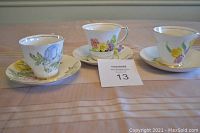 Three bone china cups with matching saucers arranged on a table, each with distinct floral patterns representing different sets.