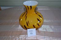 Front view of the yellow and brown streaked mouth blown glass vase with a white interior sitting on a table.