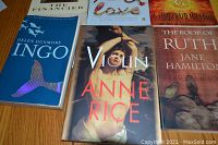 Close-up photo of several books including Ingo by Helen Dunmore, Violin by Anne Rice and The Book of Ruth by Jane Hamilton, showing cover details.
