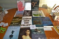 Photo of 14 hardcover books on a wooden table, showing varied titles and authors.