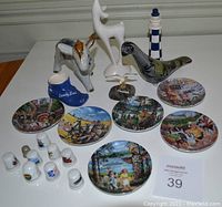 Group photo of assorted souvenirs including pottery figures (donkey, bird, deer), ceramic baseball cap, lighthouse figurine, and nine small decorative plates with Canadian scenes.