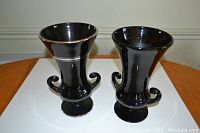 Front view of two black amethyst urn style vases with curved handles and silver trim on one vase.