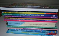 Stack of teaching resource books including art activities, classroom strategies, and children's activity books.