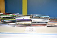 Photo showing multiple stacks of assorted music CDs on a white surface against blue and yellow background.