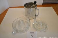 Two glass lemon juicers and metal flour sifter grouped on wooden surface.