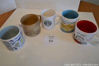 Five Starbucks mugs of various designs and sizes shown on table