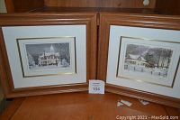 Two framed winter scene prints titled 'Sleigh Ride' and 'The Gather' by Walter Campbell, placed side by side on a table, with visible certificates on back of frames.