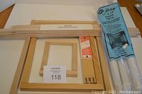 Set of assorted wood needlepoint stretcher frames in various sizes and a new unopened Snap Square Frame in blue packaging on a table.