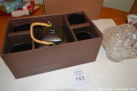 Tea set in original packaging box containing black teapot with rattan handle and four matching cups, with crystal candy dish beside box.