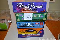 Stack of five board games including Trivial Pursuit Genus IV, Outburst, Cranium, Thinkblot, and Balderdash, showing box side labels.