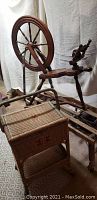 Full view of reproduction wooden spinning wheel next to the vintage sewing basket.