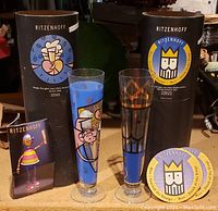 Two Ritzenhoff collectable glasses displayed with original packaging tubes and a small promotional card.