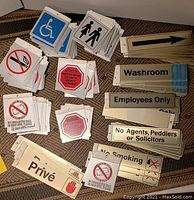 Image of assorted new metal and laminated plastic retail signs including handicap symbols, no smoking, employees only, directional arrows, and warning notices.