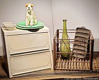 Photo showing white metal bread box with two compartments, green bottle inside rusty steel crate, cast iron cornbread mold, and dog statue