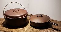 Photo of two vintage cast iron pots together: one with a handle and lid labeled Findlay, the other a skillet with lid and handle, both rusty