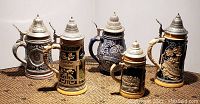Front view of five German beer steins, showing detailed scenes and pewter lids