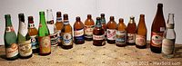 Photo showing full lineup of 17 vintage beer bottles in various colors and label conditions, some with partial paper labels