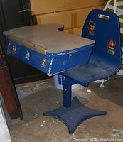Blue vintage children's desk with attached chair and flip-up top showing wear and vintage stickers on chair back.