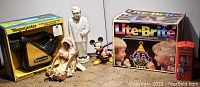 Overall view of lot showing all collectible toys including Magnajector projector in box, Eskimo doll, Colonel Sanders figurine, Mickey Mouse figurine, and Lite-Brite box