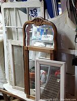 Three mirrors and three vintage window frames arranged together. Mirrors include white and brown frames with carved details; windows are white, multi-paned with some paint wear.