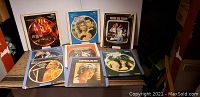 Photo showing 8 RCA VideoDiscs in cardboard sleeves featuring various musical artists and movies from the 70s and 80s placed on a surface.