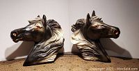 Both vintage plaster horse heads shown side by side on a tan textured surface, well lit to highlight detailing and size.