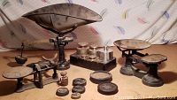 Photo showing three vintage mechanical balance scales with multiple metal weights in front and on a stand