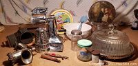 Photo showing multiple vintage kitchen and misc items including nut grinder, glass cake dome, mixing bowl, metal meat grinder attachment, spice jars, and small tools