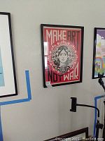 Close-up of 'Make Art Not War' framed print in black frame, hanging on wall