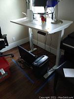 White electric height-adjustable desk with white top, metal legs and control box under surface