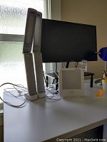 Photo of two identical tall white light therapy lamps and one smaller Verilux light therapy lamp in front of a Samsung monitor on a desk.