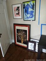 View of five framed art prints leaning against wall, showing variety of colors and styles