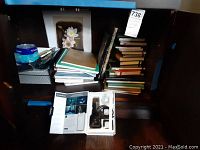 Shelf showing stack of books and notebooks, blank DVDs, and some loose items