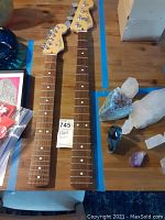 Two guitar necks laid on a wooden table showing full fretboards and headstocks alongside various crystals.