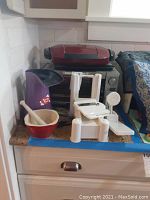 Photo showing red Air Crazy popcorn maker, Breville toaster oven, white plastic vegetable slicer, stone mortar and pestle on countertop.