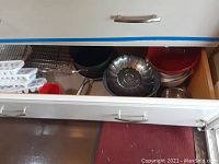 Drawer with multiple kitchen items including ice trays, cooling racks, red and white mixing bowls, a metal bowl, and bakeware