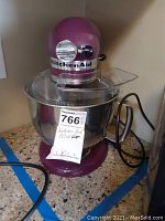 Front view of plum KitchenAid mixer on countertop with bowl and whisk.