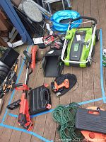 Photo showing all tools and equipment including lawn mower, weed eater, drills, jigsaw, and battery charger arranged on deck floor