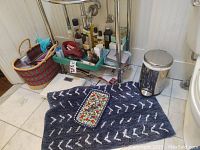 Photo showing a collection of personal care bottles including shampoos, conditioners, lotions, sample perfume, deodorant, toothpaste, along with hair dryer, clips, makeup bags, personal mirror, scale, bath rug, and a stainless steel trash can.