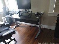Front view of the desk showing motorized legs, black tabletop, Samsung monitor, monitor riser, cooling pad and Herman Miller chair