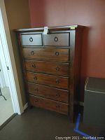 Front angle view of the tall wooden dresser showing drawer fronts and metal ring handles.