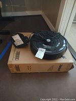 Side angle showing the Roomba vacuum on top of the box with charging dock and power cord.