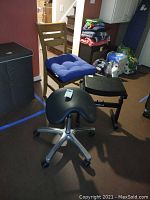 Wood chair with blue cushion, black ergonomic stool on wheels, and small black wooden stool arranged in a room corner.
