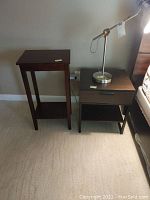 View of narrow wood side table and one end table with a lamp on top, showing walnut finish and modern style drawer handle.